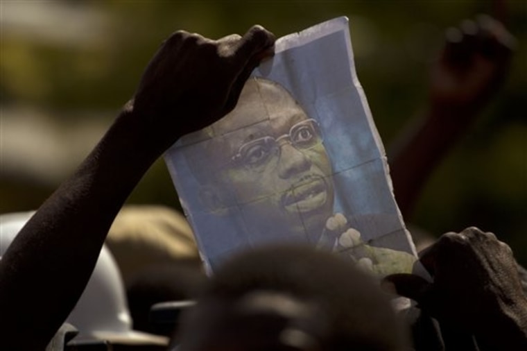 A demonstrator holds up a picture of ousted Haitian President Jean-Bertrand Aristide during a protest against Haiti's President Rene Preval in Port-au-Prince, Haiti, on Monday. Preval's term had been scheduled to end Monday but will stay in office for three more months as his country chooses a successor in a delayed election, said his chief of staff. 